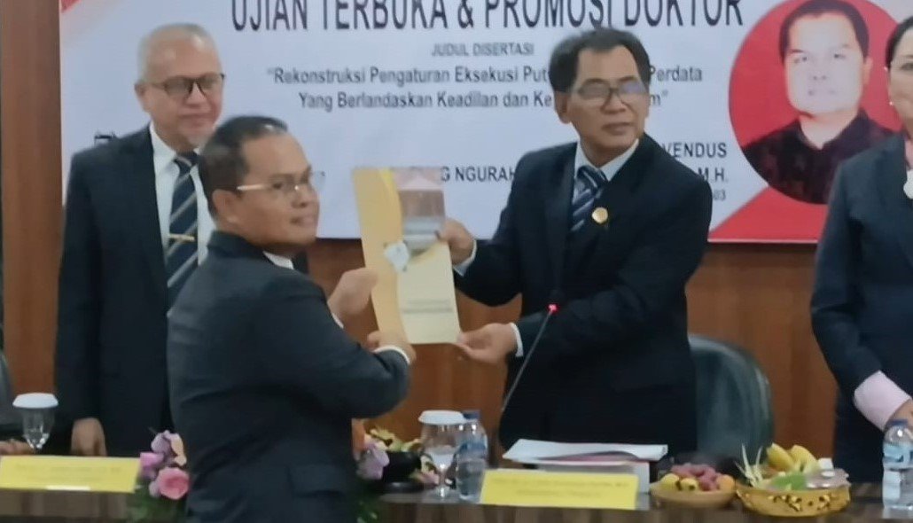 LULUS DOKTOR - Rektor Unwar Prof. Dr. Ir. I Gde Suranaya Pandit, M.P., yang juga Ketua Sidang sekaligus Penguji IX, menyampaikan tanda kelulusan sebagai doktor ke-27 Fakultas Pascasarjana Unwar, Denpasar, bagi AA Alit Wiraputra, usai ujian terbuka pada Kamis (26/3/2026). (BIG.com/ist)