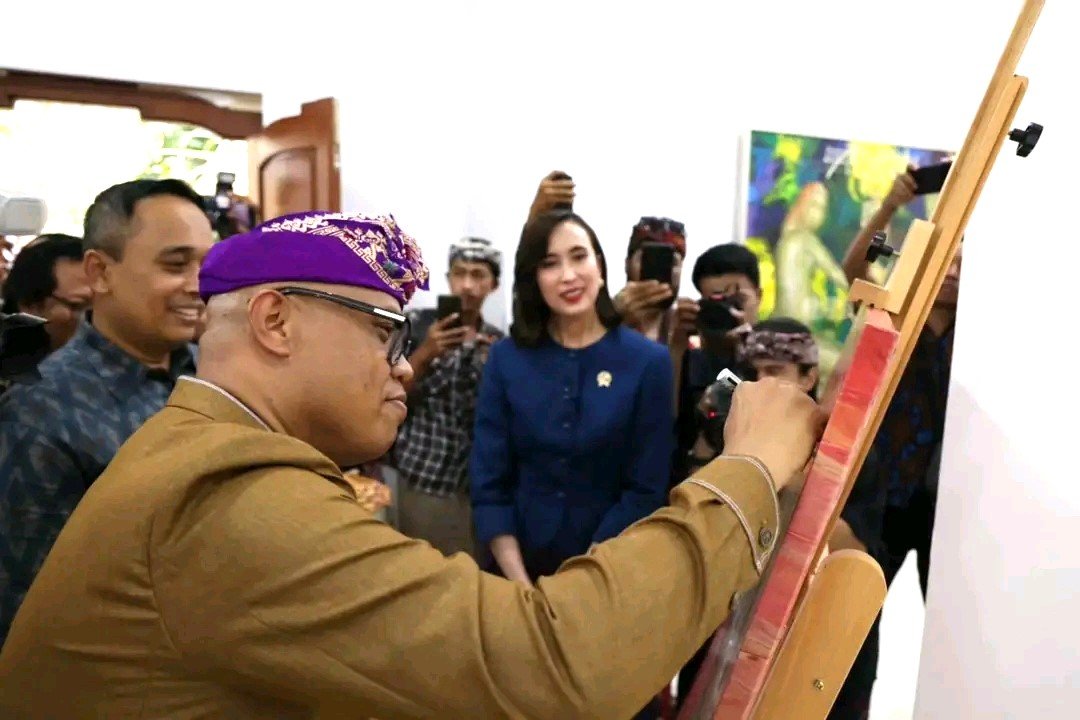 BUBUHKAN TANDA TANGAN - Wayan Kun Adnyana membubuhkan tanda tangan dikanvas menandai pameran lukisan karyanya di Nata-Citta Art Space (N-CAS), Institut Seni Indonesia Bali (ISI Bali) yang dibuka Menteri Pariwisata (Menpar) Widiyanti Putri Wardhana pada Rabu (25/3/2026).(BIG.com/ist) 